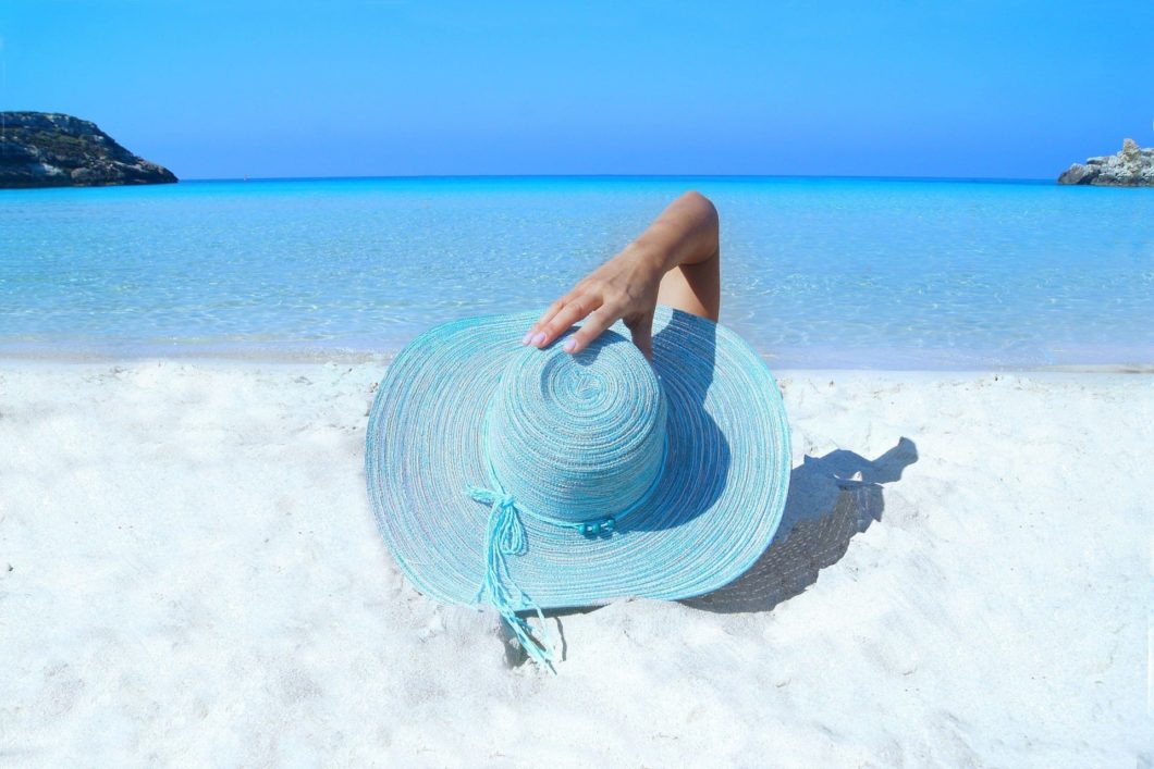 Kvinna med blå solhatt på en vit strand och blått hav